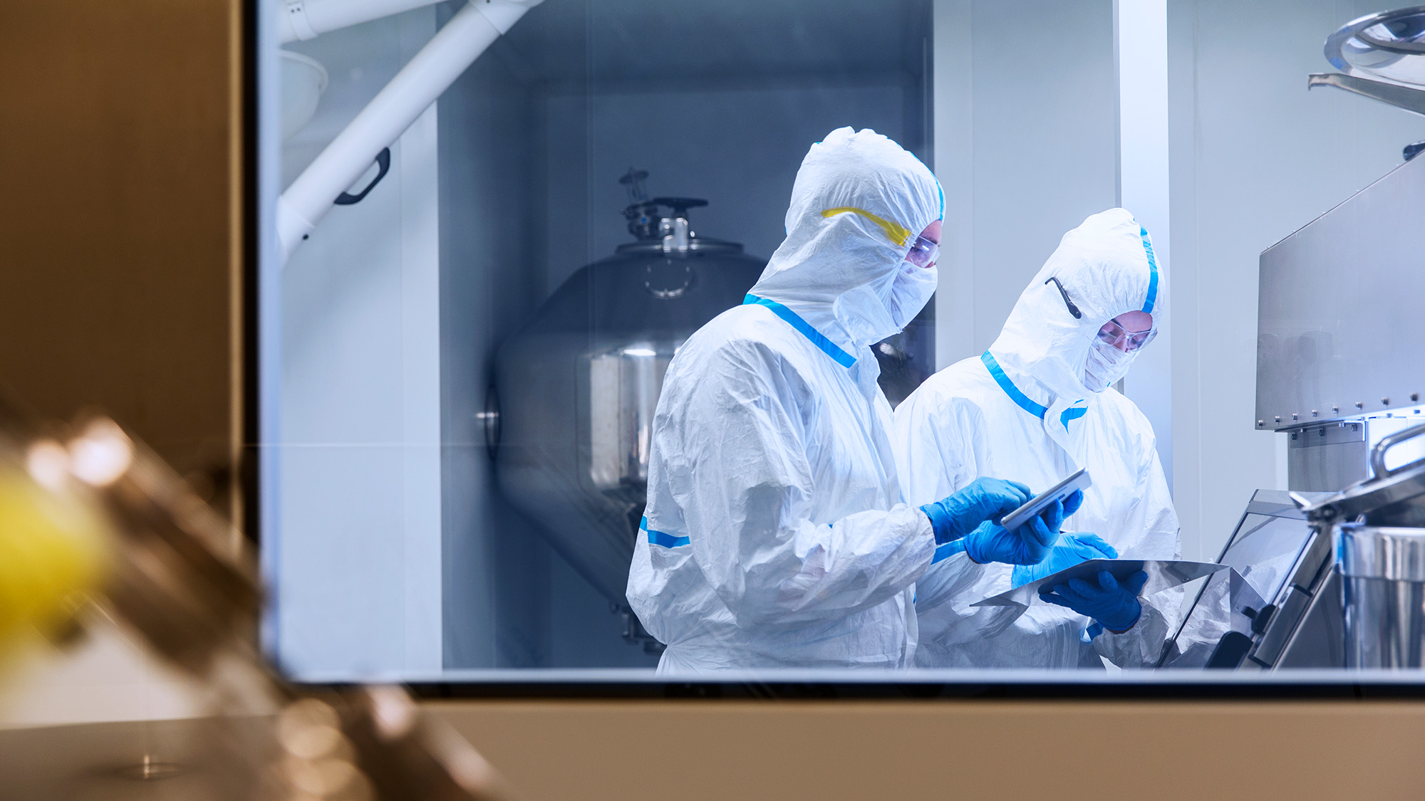 Scientists in cleanroom suits using digital tablets during a laboratory experiment