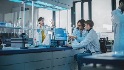 Researchers in lab coats looking at analytical data on computers at the LaCoMeD laboratory, part of Intertek Analytical Services in France.