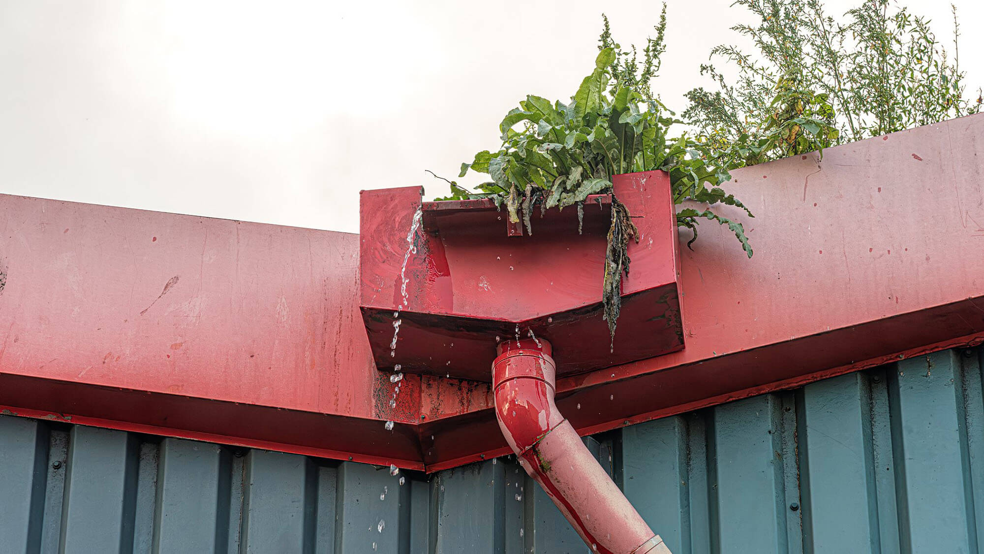 red rainwater drain system and downspout where the water leaks over the edge of the drain